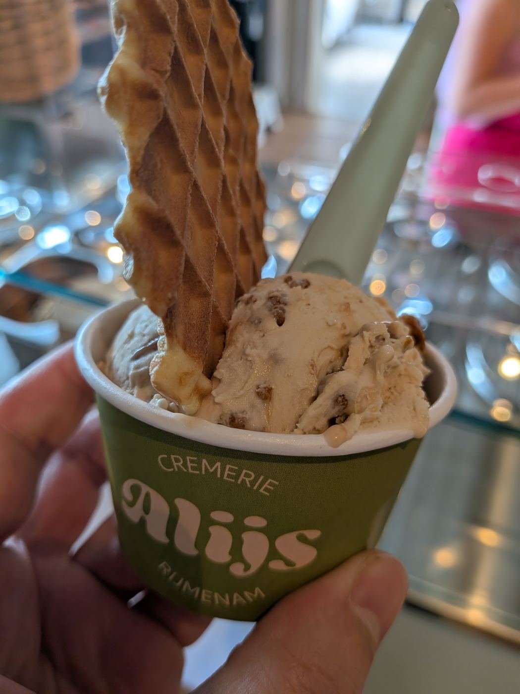Een groen Alijs-bekertje met ijs en een wafeltje, in de hand